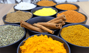 Colorful assortment of spices in bowls with cinnamon sticks on a wooden surface.